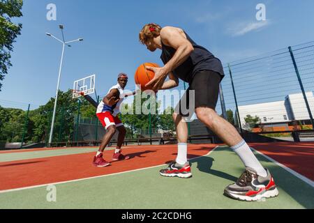 Young sportsmen playing basketball at outdoor court on sunny summer day Stock Photo