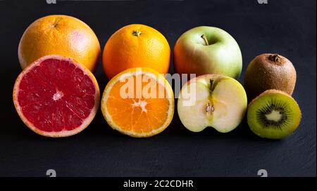 Fresh whole and cut fruit, orange, apple, kiwi, grapefruit on black Stock Photo