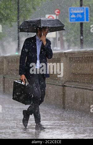 A man shelters from heavy rain under an umbrella in London as violent thunderstorms swept across the north of England and Scotland, causing flash flooding in places. Stock Photo