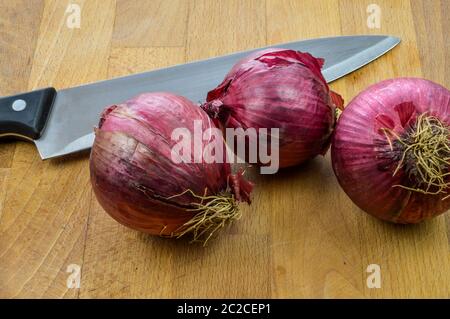 Red Onions on a wooden cutting board with kitchen knife close up, Tropea red onions. Stock Photo
