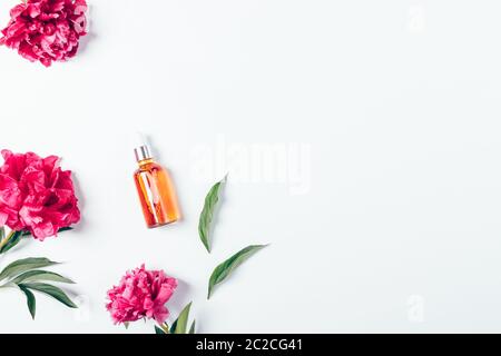 Floral flat lay composition bottle beauty serum next to peony flowers on a white background with copy space. Stock Photo