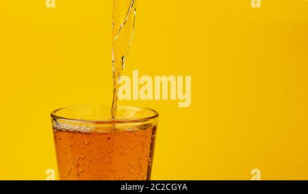 Apple juice pouring into glass, isolated on yellow background Stock Photo