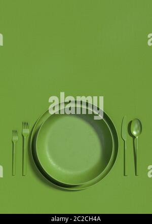 Empty green plate and cutlery on a green table. Monochrome vertical illustration of a table serving on a top view. Copy space. 3D rendering Stock Photo