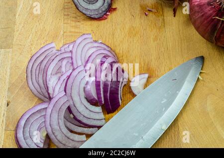 Slicing Red Onions on a wooden cutting board with kitchen knife close up, Tropea red onions. Stock Photo