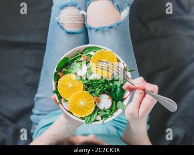 Woman in jeans at bed, holding vegan salad bowl Stock Photo