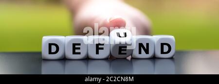 Hand turns dice and changes the word "defend" to "defund". Stock Photo