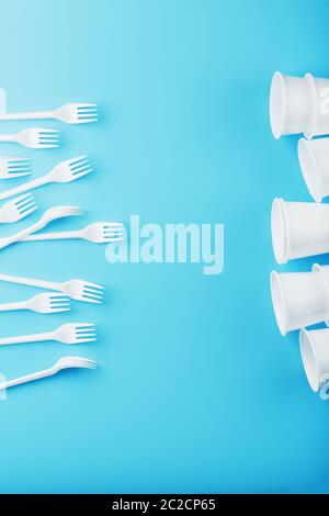 Plastic tableware on a blue background. Disposable forks and glasses with free space. Stock Photo