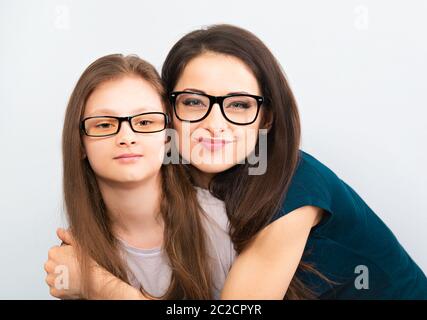 Happy young casual mother and smiling kid in fashion glasses hugging on light blue background with empty copy space. Closeup studio portrait Stock Photo