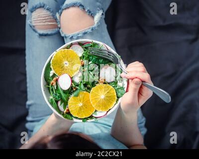 Woman in jeans at bed, holding vegan salad bowl Stock Photo