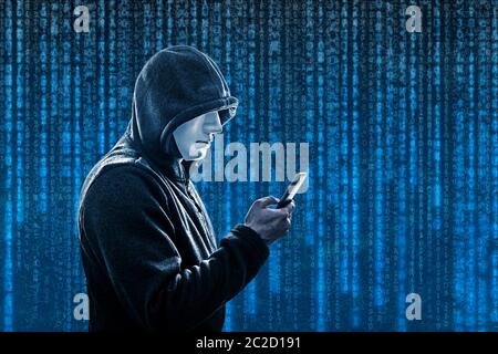 Hooded hacker with mask holding smartphone Stock Photo