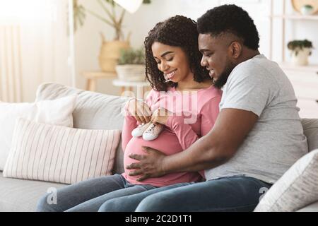 Happy pregnant couple putting future baby little boots on tummy Stock Photo