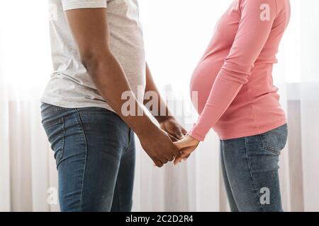 Black expecting couple holding hands, standing against each other Stock Photo