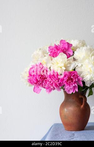 Beautiful bouquet of peonies in a clay pot stands on a table with a blue linen tablecloth Stock Photo