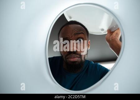 Under the lid of the toilet. African-american man looking for job in unusual places at his home. Crazy, funny way to find career and going up. Concept of crisis, unemployment, finance, business. Stock Photo