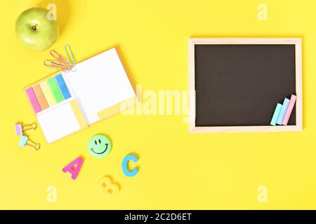 Chalkboard with wooden frame and colorful chalks and school stationeries, isolated on yellow background. Stock Photo