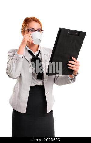 A portrait of a businesswoman drinking from a cup and looking at a clipboard, isolated on white background. Stock Photo