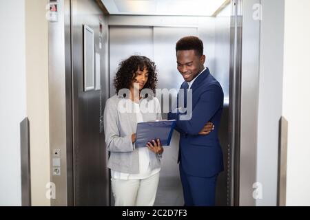 Businesspeople Discussing Standing Inside Elevator At Work Stock Photo