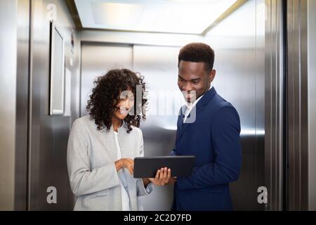 Businesspeople Discussing Standing Inside Elevator At Work Stock Photo