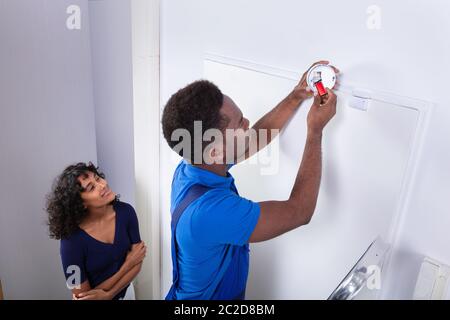 Repairman Changing Battery In Smoke Detector On Wall At Home Stock Photo