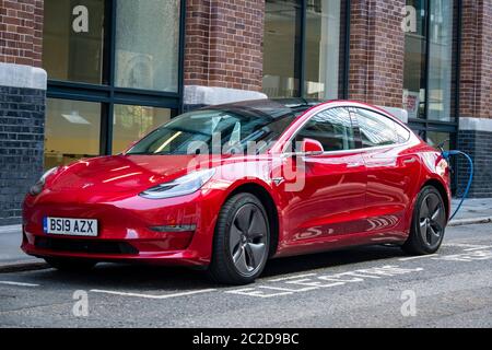 LONDON, JUNE, 2020: A red Tesla Model 3 parked and charging on city street Stock Photo