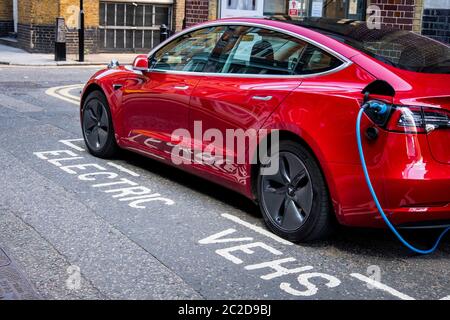 LONDON, JUNE, 2020: A red Tesla Model 3 parked and charging on city street Stock Photo