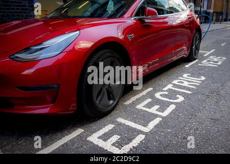 LONDON, JUNE, 2020: A red Tesla Model 3 parked and charging on city street Stock Photo