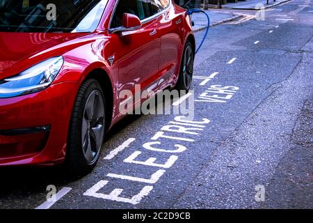 LONDON, JUNE, 2020: A red Tesla Model 3 parked and charging on city street Stock Photo