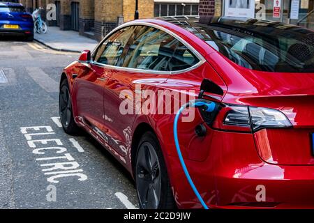 LONDON, JUNE, 2020: A red Tesla Model 3 parked and charging on city street Stock Photo