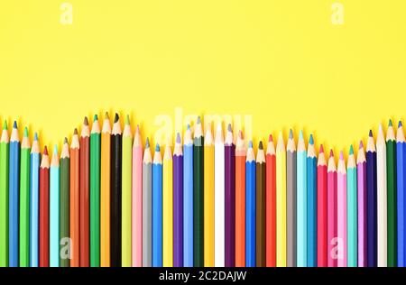 Colorful coloring pencils displayed in a wave on yellow background. Stock Photo