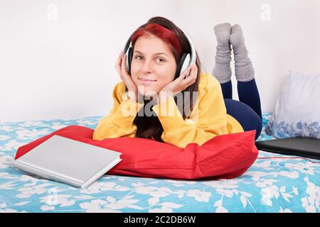 Music break after a long day of studying. Beautiful young girl lying in bed, listening to music after studying. Stock Photo