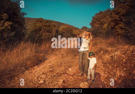 Young mother with little son walking on the trail in the mountains, camping in wild nature, active sportive family Stock Photo