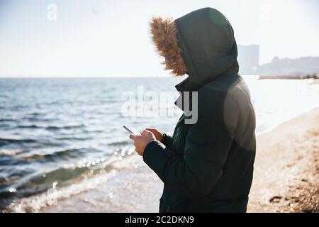 Young man using smartphone while standing by the sea Stock Photo