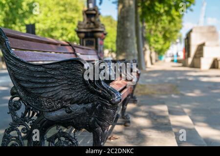 Cast iron wooden slat bench on the Embankment  adorned with a black winged Sphinx head majestically overlooking the River Thames in London, England on Stock Photo