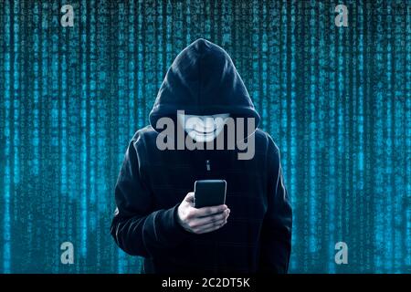 Hooded hacker with mask holding smartphone Stock Photo