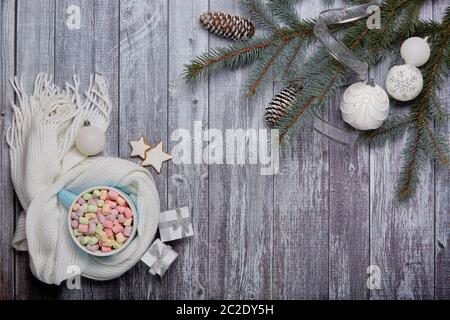 Mug of cocoa with marshmallow, woolen white scarf, gift boxes, fir tree branches and Christmas ornaments on grey wooden background. Top view with copy Stock Photo