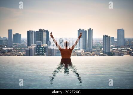 Back view of happy freedom man with raised arms enjoy his summer vacation on swimming pool Stock Photo