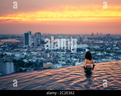 Young woman relax in swimming pool on roof top during amazing sunset and enjoy cityscape Stock Photo