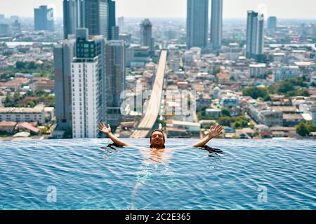 Young happy man relax on the edge of swimming pool in roof top of hotel Stock Photo