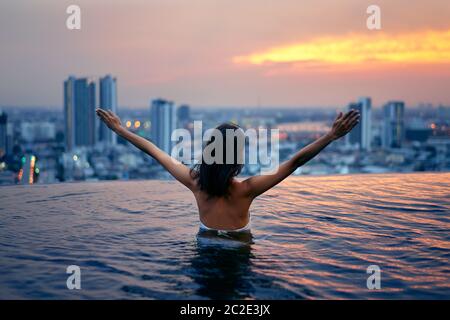 Back view of happy freedom woman with raised arms enjoy her summer vacation on swimming pool