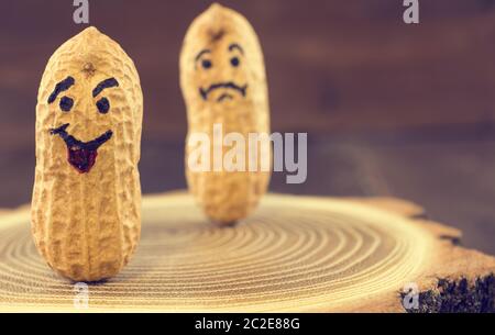 Smile and sad face drawn on dried peanuts on wooden background. Concept for good mood or bad mood Stock Photo