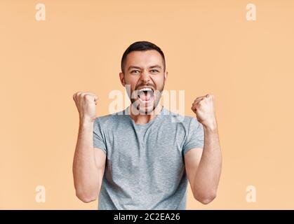 Happy man celebrating his success with winner gesture on beige background Stock Photo