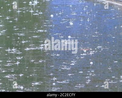 Abstract of heavy rain falling on a pond, where there is reflected purple light across two thirds of the photo in contrast to the dark water. Stock Photo
