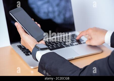 Businessman using smart watch and mobile phone and laptop computer Stock Photo