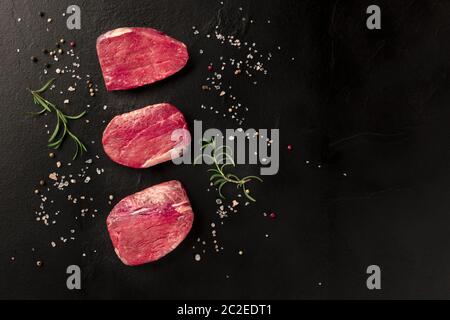 Raw beef steaks with salt, pepper and rosemary on a black background Stock Photo