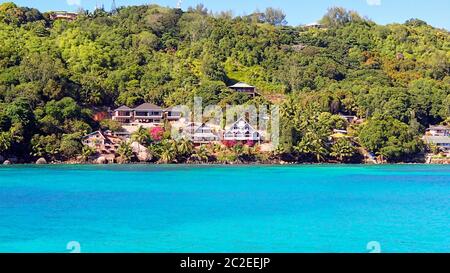 Houses and green vegetation on the coastline of the seychelles as seen from the azure blue waters Stock Photo