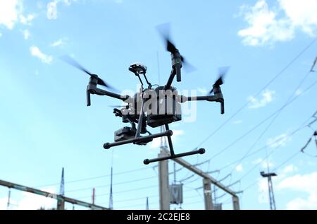 Pro quadcopter with camera aboard flying in a sky, electric pylon, cables and insulators on the background Stock Photo