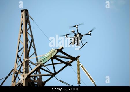 Pro quadcopter with camera aboard flying in a sky, electric pylon, cables and insulators on the background Stock Photo