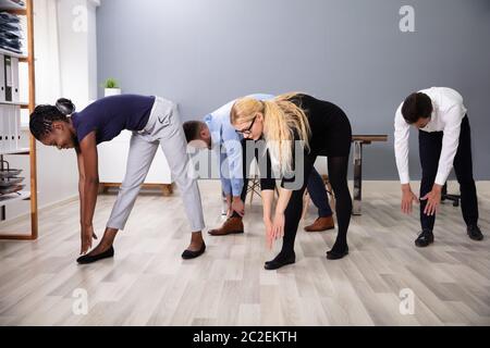 Group Of Young Businesspeople Doing Stretching Exercise In Office Stock Photo