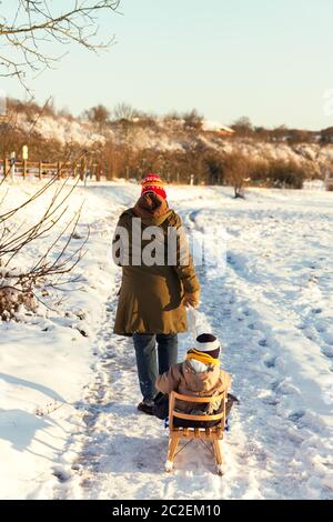 Little toddler walking outdoors in a snowy winter scene with his mom. Stock Photo