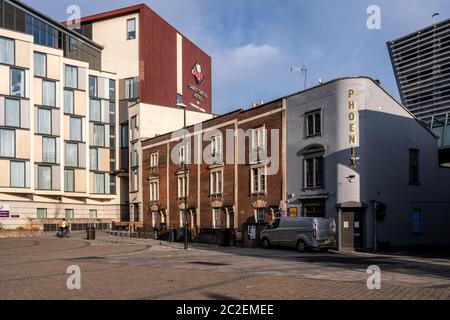 A cyclist rides through Champion Square beside the modern Cabot Circus shopping centre and traditional terraced houses and pub in central Bristol. Stock Photo